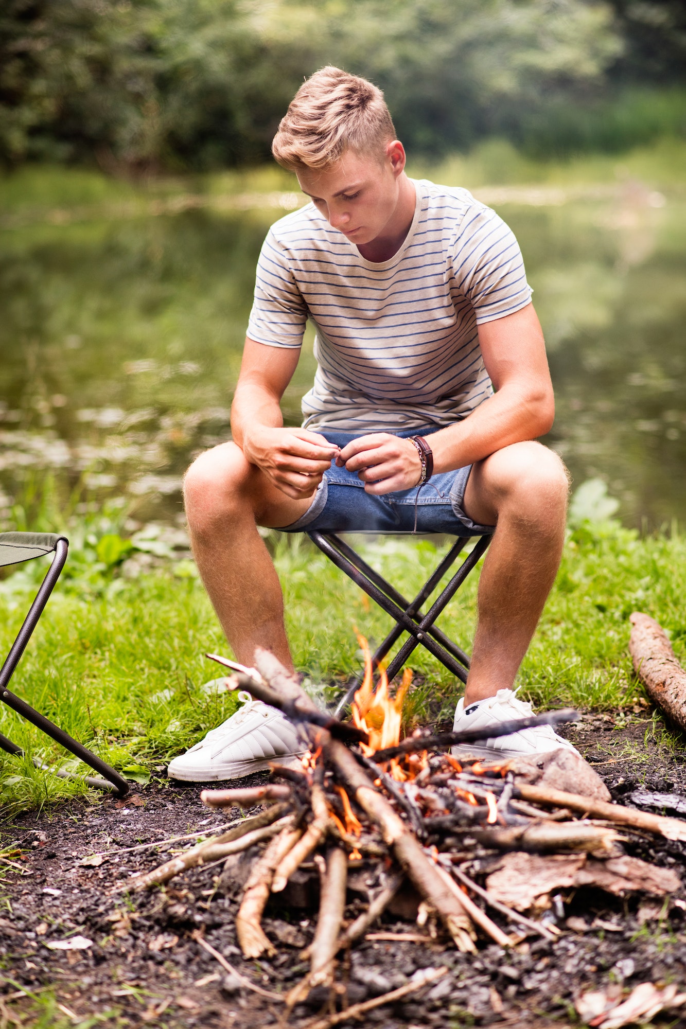Boy camping in nature, sitting at bonfire.